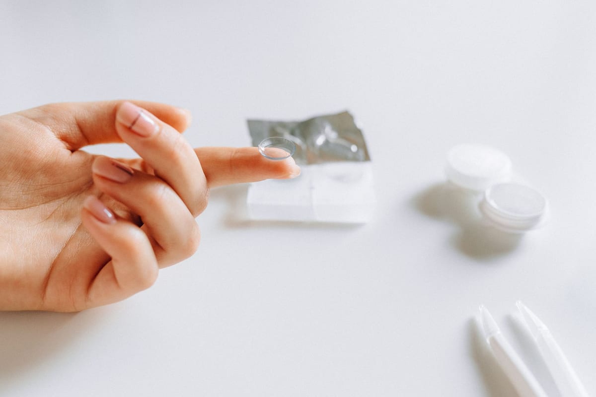 A contact lens balanced on a fingertip beside its case